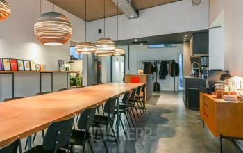 Spacious office interior at Prins Hendrikkade 48 A in Amsterdam Center, featuring a long wooden table, pendant lighting, and kitchenette area. Ideal for office space rental with a stylish, collaborative workspace vibe.