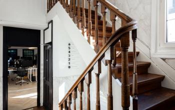 Spacious office interior at Rokin 46-1 in Amsterdam Center, featuring a wooden staircase and a glimpse of open workspaces in the background, ideal for office space rental.