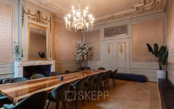 Elegant office space rental at Rokin 46-1, Amsterdam Center, featuring a spacious conference room with a long wooden table, ornate chandelier, and decorative moldings. Ideal for professional meetings.