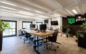 Spacious workspaces at Rokin 46-1 in Amsterdam Center featuring modern desks, office chairs, multiple computer setups, large windows with natural light, and indoor plants. Ideal for those looking for office space rental.