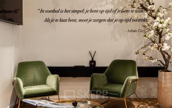 Modern, stylish reception area at Rokin 46-1, Amsterdam Center featuring green armchairs, a glass coffee table, and decorative wall art. Ideal for office space rental.