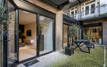 Exterior view of the office located at Groenmarktkade 5-H, Amsterdam Center, featuring modern glass doors and a small outdoor seating area, suitable for office space rental.