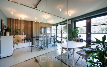 Modern office space rental at Groenmarktkade 5-H, Amsterdam Center, featuring a stylish furnished interior with glass partitions, round tables, and seating, ideal for collaborative meetings and creative workspaces.