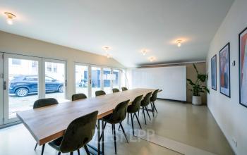 A bright conference room in Groenmarktkade 5-H, Amsterdam Center, featuring a long wooden table with green chairs, minimalist decor, and a large whiteboard, ideal for office space rental.