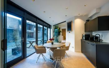 Modern office space in Amsterdam Center featuring a bright area with a round table and chairs, surrounded by glass doors leading outside. Ideal for collaboration or small meetings.