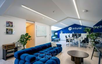 Modern office space rental at Groenmarktkade 5-H, featuring a stylish blue sofa, sleek desks with computers, and accent plants in Amsterdam Center.