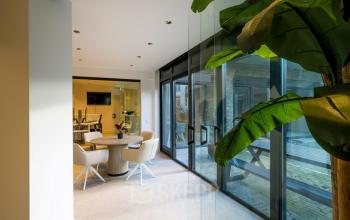 Modern office space at Groenmarktkade 5-H, Amsterdam Center, featuring a glass-walled conference room with a round table and comfortable chairs, ideal for office space rental.