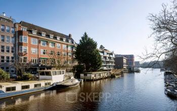 Canal-side view of Amsterdam Center's Groenmarktkade 5-H, showcasing nearby residential buildings and moored boats, perfect for those seeking office space rental in a picturesque setting.
