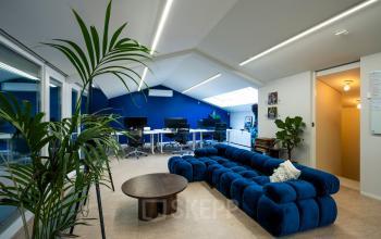 Modern office interior at Groenmarktkade 5-H, Amsterdam Center, featuring a plush blue sofa and workstations with natural light, suitable for office space rental.