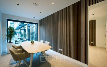 Modern office interior at Groenmarktkade 5-H, Amsterdam Center, featuring a stylish meeting area with a wooden accent wall and contemporary furniture, available for office space rental.