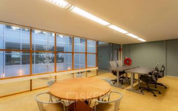 Bright office space for rent at Kerkstraat 204, Amsterdam Center, featuring large windows, desks, and chairs. Ideal for collaborative work.