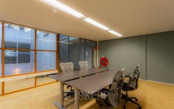 Modern office space with a large table and ergonomic chairs, perfect for collaborative work. Bright windows allow natural light, creating an inviting atmosphere for productivity. Ideal for businesses looking for office space rental in Amsterdam Cente