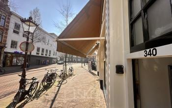 Exterior view of an office located at Nieuwezijds Voorburgwal 340 in Amsterdam Center, showcasing a street with bicycles and buildings under a bright sky, perfect for office space rental.