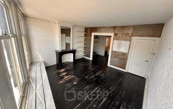 Spacious room with dark wooden floors and large windows in Amsterdam Center's Nieuwezijds Voorburgwal 340, ideal for office space rental. Features a decorative fireplace and built-in shelves.