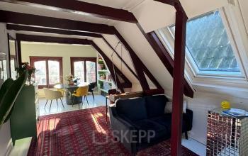 Charming office space in Amsterdam Center with sloped ceilings, red beams, a cozy dark blue sofa, and a spacious rug under natural light, ideal for office space rental.