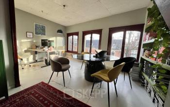 Bright office space rental at Nieuwezijds Voorburgwal 340 with multiple desks, chairs, and a central round table, complemented by large windows offering natural light and a view of Amsterdam Center.