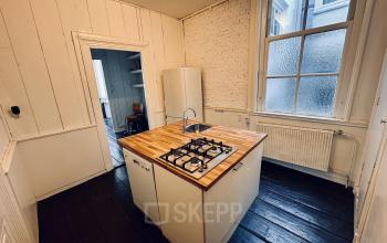 Cozy office kitchen space at Nieuwezijds Voorburgwal 340, Amsterdam Center, featuring a central island with a stove, wood countertop, and large window, perfect for cooking and informal meetings.