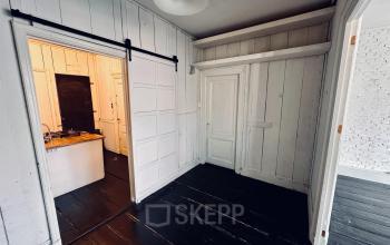 Unfurnished office space with classic wooden paneling and sliding door in Amsterdam Center, available for rent. Features dark flooring and a compact kitchenette area.
