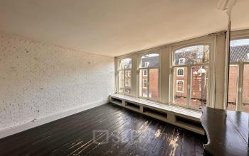 Spacious room with large windows overlooking Amsterdam Center, showing a view of historic buildings. A rustic wooden floor complements the brick walls. Ideal for open floorplan office space rental.