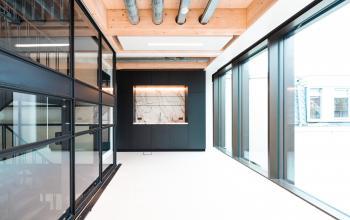 Bright office space interior with large windows, black furnishings, and exposed ceiling beams on Pieter Cornelisz. Hooftstraat 7, ideal for office space rental in Amsterdam Center.