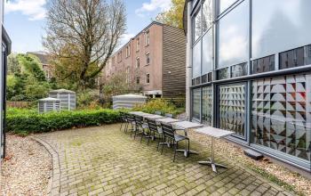 Outdoor view of office space rental at Stadhouderskade 55 in Amsterdam Center featuring a brick patio with tables and chairs, surrounded by greenery.