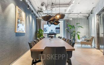 Conference room at Stadhouderskade 55, Amsterdam Center, featuring modern furnishings and ample lighting. Ideal office space rental for meetings. Sleek design with a long table and chairs, accented by plants.