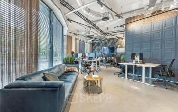 Modern office space at Stadhouderskade 55 in Amsterdam Center with employees working at computers and a seating area with a sofa and table. Ideal for office space rental.