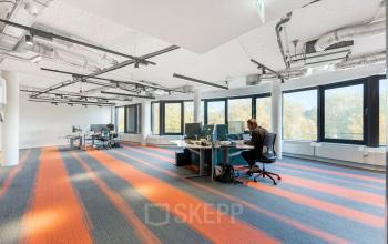Modern office space at Stadhouderskade 55 in Amsterdam Center with large windows and bright flooring, featuring a person working at a desk. Ideal for office space rental.