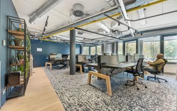 Bright office space at Stadhouderskade 55, Amsterdam Center, featuring several workstations and modern decor, available for rent. A person is seated and working at a desk.