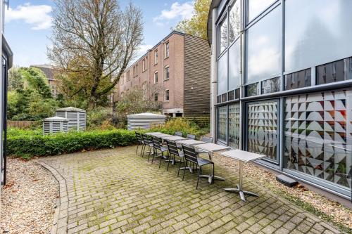 Outdoor view of office space rental at Stadhouderskade 55 in Amsterdam Center featuring a brick patio with tables and chairs, surrounded by greenery.