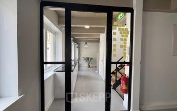A modern office space to rent at Kloveniersburgwal 131K, Amsterdam Center. The interior is furnished with a sleek glass door, natural light, and contemporary design elements.