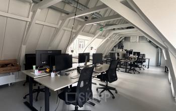 Spacious, modern office space with multiple workstations and ergonomic chairs under vaulted ceilings, available for rent at Kloveniersburgwal 131K, Amsterdam Center.