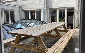 Outdoor wooden picnic tables on a deck outside an office space for rent at Kloveniersburgwal 131K in Amsterdam Center.