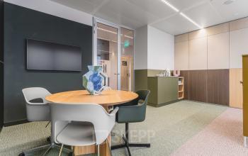 Office space at Piet Heinkade 55, Amsterdam Center, featuring a round table with chairs, wall-mounted screen, and cabinet for office space rental.