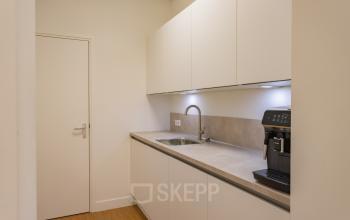 Simple kitchen area in an office with white cabinets and a coffee machine, suitable for office space rental.