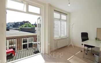 Bright office space with desk and chair facing a balcony at Warmoesstraat 149-151 in Amsterdam Center. Ideal for office space rental, featuring large windows and a minimalistic design.