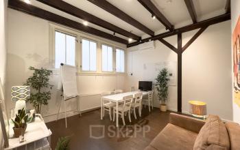 Charming office space rental at Warmoesstraat 149 - 151, Amsterdam Center, featuring a cozy meeting area with a sofa, whiteboard, and plant accents under exposed beams.