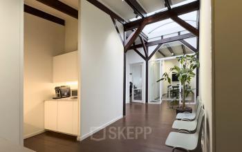 Bright office interior at Warmoesstraat 149-151, Amsterdam Center, featuring white walls, wooden beams, and a small kitchenette, offering perfect office space rental opportunities.
