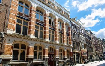 Exterior view of a historic office building at Warmoesstraat 149-151 in Amsterdam Center, showcasing classic architecture with brick and large windows, ideal for office space rental.