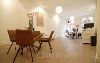 Modern office space rental at Warmoesstraat 149-151, featuring a well-lit room with wooden floors, contemporary furniture, and large windows.