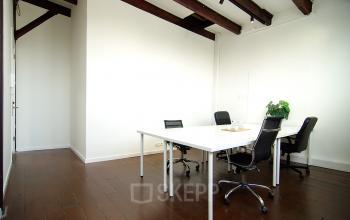 A well-lit office space rental at Warmoesstraat 149 - 151 in Amsterdam Center, featuring a clean white table, chairs, and wooden flooring.