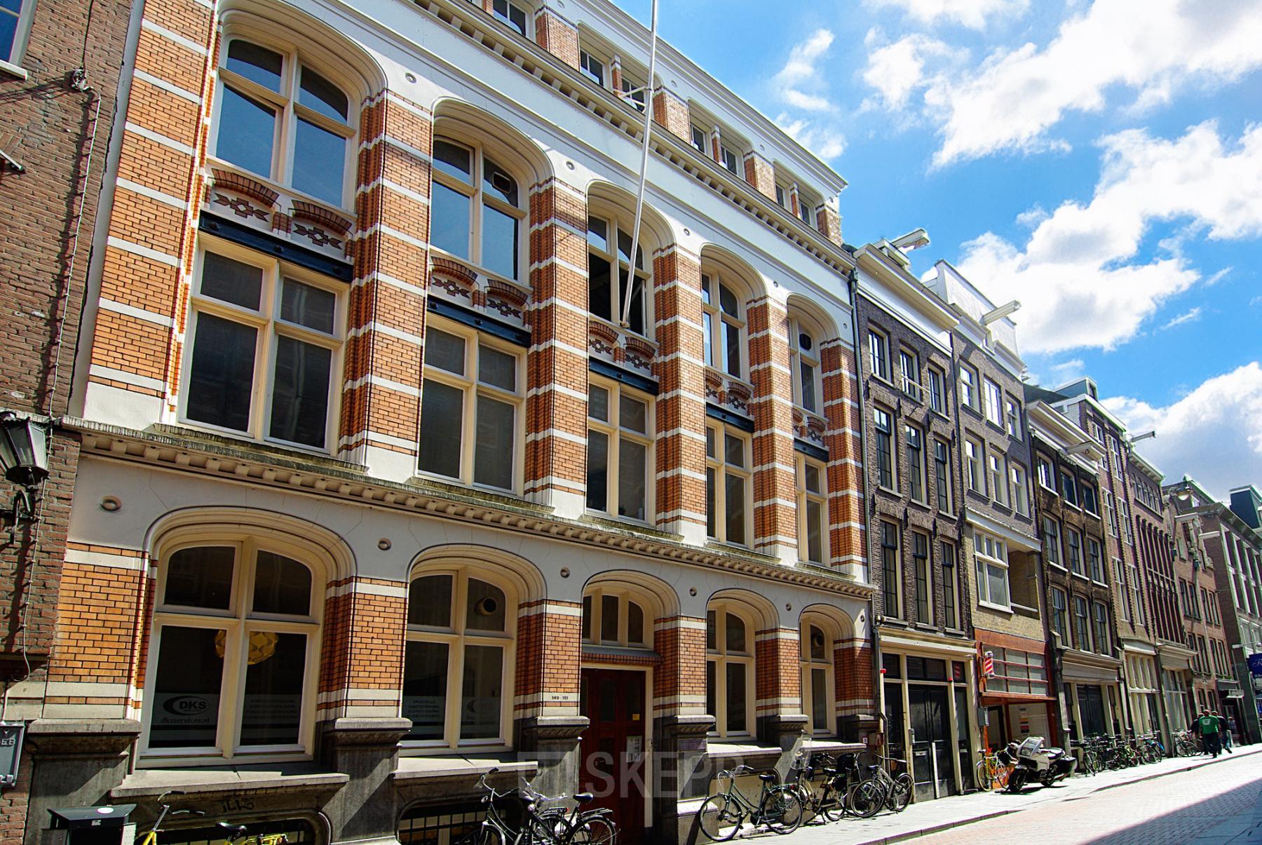 Exterior view of a historic office building at Warmoesstraat 149-151 in Amsterdam Center, showcasing classic architecture with brick and large windows, ideal for office space rental.