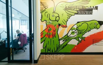 Bright office space rental at Weteringschans 165, Amsterdam Center, with a vibrant wall mural and a person engaged in work at their desk.