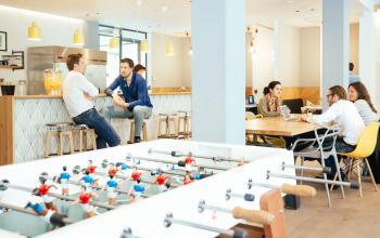Modern office space rental at Weteringschans 165, Amsterdam Center, featuring a foosball table, casual meeting areas, and professionals engaged in discussions.