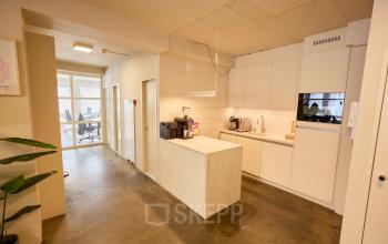 Bright office space with a kitchenette in Amsterdam Center, featuring modern furnishings and a glimpse of the workspaces area. Ideal for office space rental.