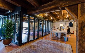 Interior of an office with a spacious workspace, wooden beams, glass walls, and modern furnishings located at 's-Gravenhekje 1A, in Amsterdam Center. Office to rent with an open floor plan and natural light.