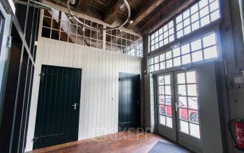 Entrance area of office space for rent at 's-Gravenhekje 1A, Amsterdam Center, with wooden floors, black and white doors, and large windows.