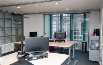 Dual workstations in a bright office space at Zuiderkerkhof 72, Amsterdam Center, with modern decor and large windows offering city views, ideal for office space rental.