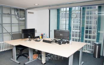 Modern office space for rent at Zuiderkerkhof 72, Amsterdam Center, featuring large windows and equipped workstations for two.