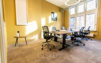 Bright office space with four workstations, modern chairs, and a small side table near large windows at Nieuwezijds Voorburgwal 104-108, ideal for office space rental in Amsterdam Center.